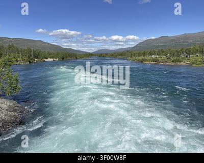 Fluss mit klarem Wasser fließt durch ein Waldgebiet unter blauem Himmel mit Bergen im Hintergrund, Sjoa, Gjendersheim, Maurvangen, Jotunheimen, Norwa Stockfoto