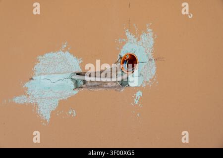 Nahaufnahme eines orangefarbenen elektrischen Anschlusskastens mit Drähten und einem Kabelrohr, das während der Bau- oder Reparaturarbeiten in eine Wand eingebettet ist Stockfoto