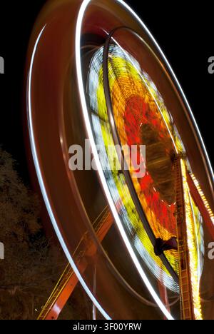 Zeitbelichtung bei Nacht, die die Patten in einem rotierenden Riesenrad zeigt, das durch die Lichter, Farben und Anordnung der Lichter auf dem drehenden Rad erzeugt wird. D Stockfoto