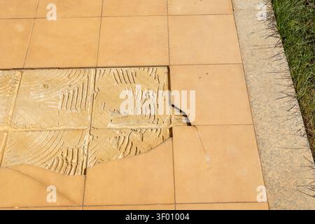 Nahaufnahme von gebrochenen terrakottafarbenen Pflasterplatten an einem sonnigen Tag, die den rauen Betonuntergrund darunter freilegen Stockfoto