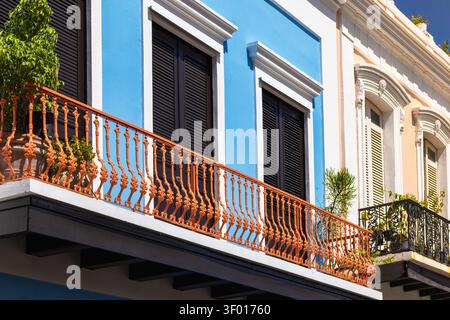 Detaillierte, flache Sicht auf die in hellen Blau und Pastellpfirsichfarben gehaltenen historischen Gebäude in Old San Juan mit verzierten orangenen und schwarzen schmiedeeisernen Balkonen Stockfoto