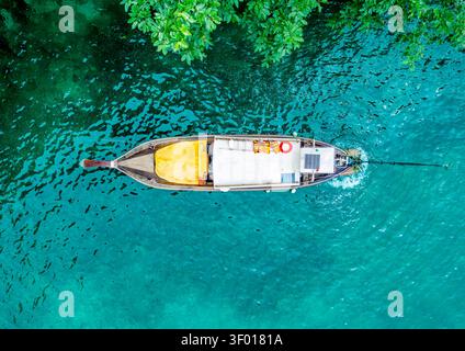 Blick von oben auf ein thailändisches Longtail-Boot, das im Sommer über das kristalltürkisfarbene Meer in der Nähe von Koh Tao, Thailand, gleitet, mit üppigen Uferblattflächen Stockfoto