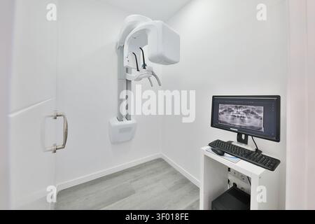 Sauberer, moderner Raum für die zahnärztliche Radiologie mit einem Panorama-Röntgenscanner und einem Computermonitor, der ein Zahnbild anzeigt, in einem hellen klinischen Umfeld Stockfoto
