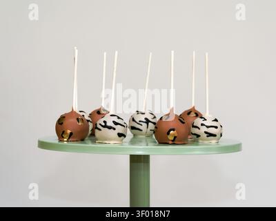 Schokoladenüberzogene Kuchenpops mit dekorativem Drizzle auf einem grünen Ständer Stockfoto