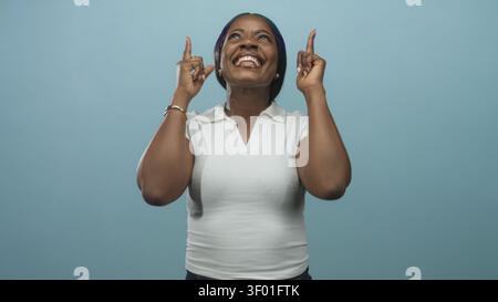 Frau im weißen Poloshirt zeigt die Zeigefinger nach oben und lächelt breit und zeigt Zähne im Studio mit türkisfarbener Kulisse; Freude feiern. Stockfoto
