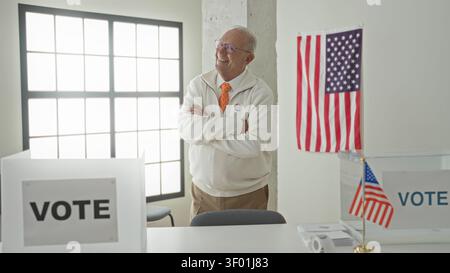 Mann mit überkreuzten Armen, mit einem „ich stimmte“-Sticker, neben einem klaren Wahlzettel und amerikanischer Flagge in einem Wahlhaus, Stolz auf die bürgerliche Pflicht. Stockfoto