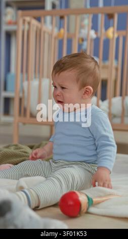 Der Junge weint und greift nach einem Spielzeug, während sich die Pflegekraft in einem Gebäude mit einem Taschentuch das Gesicht abwischt. Stockfoto