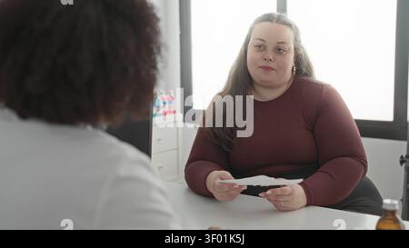 Frau, die Papier hält und ein Rezept vom Arzt über einen Kliniktisch in einem medizinischen Gebäude erhält; Sorge Vertrauen. Stockfoto