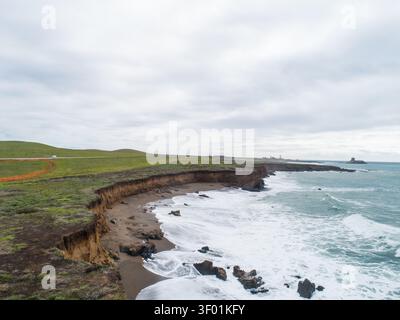 Aus der Vogelperspektive auf die zerklüftete Küste mit Sandstränden, felsigen Felsvorsprüngen und grasbewachsenen Klippen unter bewölktem Himmel in San Simeon, Kalifornien, USA. Stockfoto