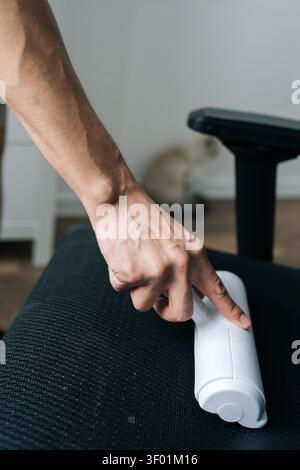 Nahaufnahme der Hand mit weißer Fusselrolle, um Tierfell und Staub von schwarzem Bürostuhl zu reinigen. Hausarbeit und Haushaltsreinigungskonzept mit Stockfoto