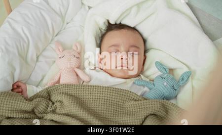 Baby schlaft in der Wiege mit sichtbarer linker Hand und zwei gestrickten Häschen-Spielzeugen auf einer weichen Decke im Kinderzimmer; ruhiger Komfort. Stockfoto