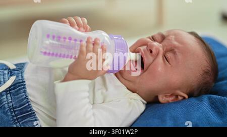 Hispanischer Junge weint, während er eine Milchflasche hält, eine kleine Hand am Brustwarzen hält und die Hand des Pflegepersonals beim Bauen hilft; Sestress Comfort Bonding. Stockfoto