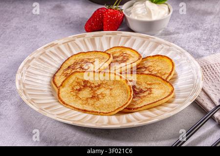 Goldene braune Pfannkuchen auf strukturiertem Teller mit frischen Erdbeeren Schlagsahne im Hintergrund. Weiches natürliches Licht hebt warme Rosttöne hervor Stockfoto