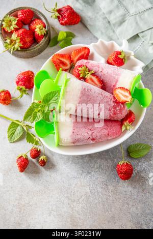 Hausgemachtes Erdbeereis auf einem Stock aus frischen Erdbeeren auf einer strukturierten grauen Steinoberfläche. Leckeres Sommerdessert zum Verzehr. Kopierbereich. Stockfoto
