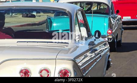 Eine Nahaufnahme eines silbernen Oldtimers mit einem blauen Oldtimer und einem roten Lkw, der dahinter fährt. Stockfoto