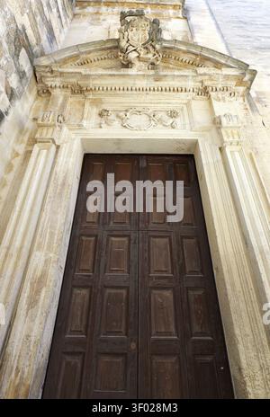 Komplizierte Steinverzierungen an einem alten hölzernen Kirchentor mit Säulen, Schnitzereien und einem alten Wappen. Italien, lecce, 18. juli 2025 Stockfoto
