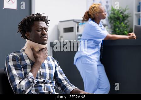 Verletzter Patient in Nackenstütze wartet leise, während er Schmerzen in der belebten Krankenhauslobby erlebt. Schwarzer Mann in gestresster Haltung mit Schweregrad und Notwendigkeit einer sofortigen ärztlichen Betreuung. Stockfoto