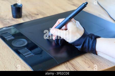 Die Designerhand trägt einen schwarzen Künstlerhandschuh mit zwei Fingern und zeichnet mit einem digitalen Stift auf einem Grafiktablett. Nahaufnahme kreativer digitaler Illustrationen Stockfoto