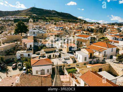Blick aus der Vogelperspektive auf das historische Dorf Pano Lefkara mit traditionellen Steinhäusern, roten Ziegeldächern und einem Kirchturm vor sanften Hügeln in Pa Stockfoto