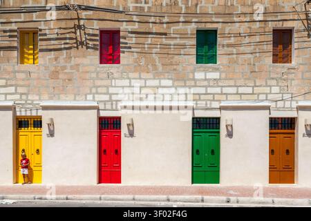 Eine Reihe von leuchtend gelben, roten, grünen und orangefarbenen Türen und Fenstern an einem weißlimestone-Gebäude in Marsaxlokk, Malta Stockfoto