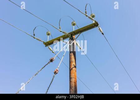 Nahaufnahme eines hölzernen Stromverteilungspunkts mit Freileitungen mit Keramikisolatoren vor klarem blauem Himmel, Abbildung e Stockfoto