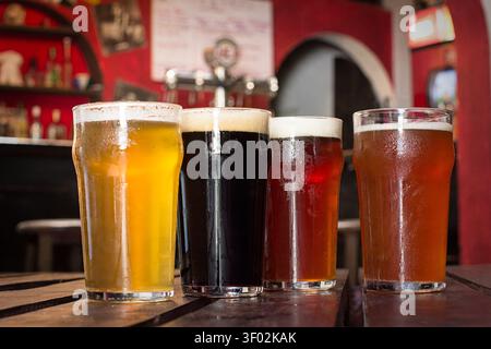 Auswahl von vier Craft-Bieren, darunter Pale Ale, Stout und Amber Beer mit cremigem Schaum, serviert auf einem Holztisch in einer Kneipe Stockfoto