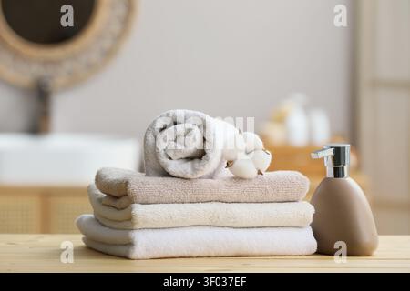 Stapel gefalteter Handtücher mit Baumwollblüten- und Seifenspender Stockfoto