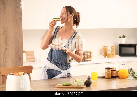 Eine junge Frau genießt Avocado-Toast in der modernen Küche Stockfoto