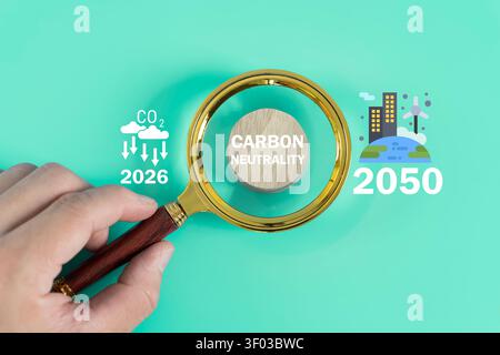 Hand mit einer Lupe über dem Text für die CO2-Neutralität mit 2050 Symbolen, die die Nettoziele, die Nachhaltigkeitsstrategie usw. darstellen Stockfoto