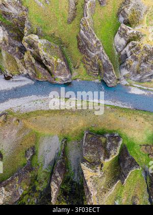 Blick aus der Vogelperspektive auf den tiefen Fjadrargljufur Canyon mit einem Fluss, der durch steile, moosbedeckte Felsformationen in Island fließt. Stockfoto