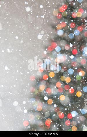 Vertikaler Weihnachtshintergrund mit weichen warmen Bokeh-Lichtern und der zarten Umrisse eines Weihnachtsbaums auf einem hellbeigen Hintergrund. Fallender Schnee Stockfoto