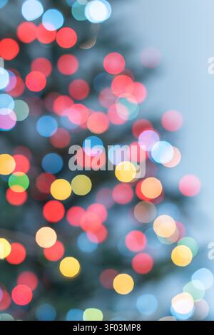 Vertikaler abstrakter Feiertagshintergrund mit bunten Weihnachtsbaum-Bokeh-Lichtern auf einem weichen hellblauen Hintergrund. Die subtile Umrisse eines Teils des Stockfoto