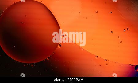 Nahaufnahme eines großen orangen Öltropfens, der in bernsteinfarbener Flüssigkeit mit kleineren Blasen aufgehängt ist und einen warmen Verlauf und weiche Reflexionen aufweist Stockfoto