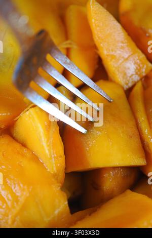 Gehackte Mangostücke mit einer Gabel auf einem kleinen Teller Stockfoto