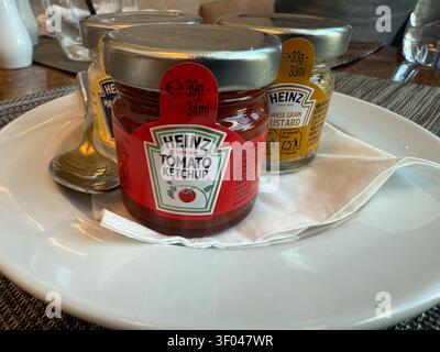 Ein Blick von oben auf Heinz Tomato Ketchup auf einem weißen Teller mit einer strukturierten Serviette in einem Restaurant, das eine neutrale Stimmung und Kommen zeigt Stockfoto