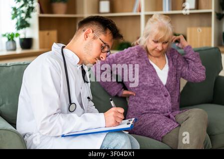 Eine ältere Frau beschreibt Beschwerden im Rücken, während sie während eines Hausbesuchs mit einem medizinischen Fachpersonal spricht. Stockfoto