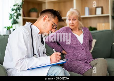 Eine ältere Frau beschreibt Beschwerden im Rücken, während sie während eines Hausbesuchs mit einem medizinischen Fachpersonal spricht. Stockfoto