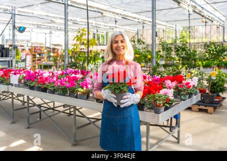 Eine ältere Gärtnerin mit einem Topf roter Blumen Stockfoto