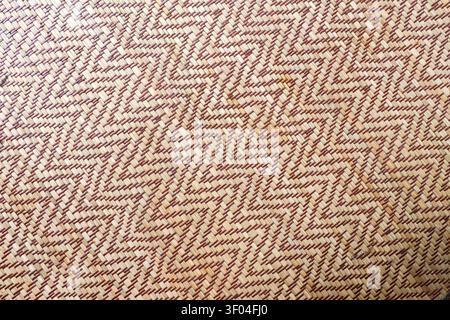 Eine gewebte Bambusmatte mit natürlichen braunen und beigen Farben, die ein Zickzack-Muster kreiert und traditionelle Handwerkskunst und organisches Material für zeigt Stockfoto