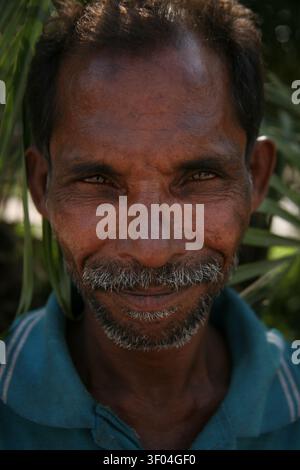 Porträt eines fröhlichen indischen Mannes, der direkt in die Kamera schaut mit einem warmen, echten Lächeln. Seine ausdrucksstarken Augen fangen das natürliche Licht. Stockfoto