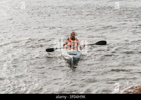 Kajakfahren Ozeanmann, der während eines aktiven Sommerurlaubs auf einem kleinen Boot auf dem offenen Meer paddelt Stockfoto