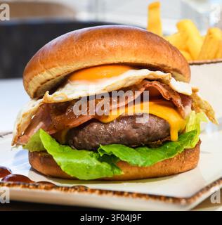 Gourmet-Beef-Burger mit Spiegelei, Speck und Käse auf einem Brioche-Brötchen Stockfoto