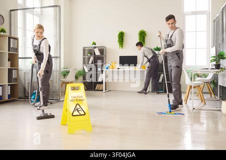 Das Hausmeisterteam wischt und saugt helles Büro mit gelbem Schild für nassen Boden Stockfoto