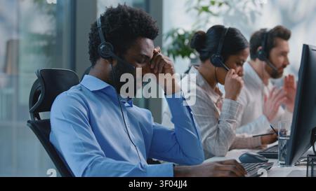 Afroamerikanischer Mann mit Kopfschmerzen streitet mit Headset-Problem müde mit schlechten erfolglosen Verkäufen Gespräch mit Kunden im Callcenter in der Nähe Stockfoto