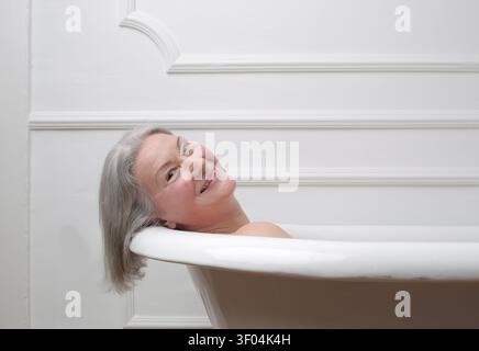 Glückliche Seniorin mit grauem Haar, die sich in einer Badewanne entspannt Stockfoto