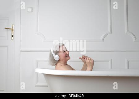 Glückliche Seniorin mit Kopfhörern, die ein Bad genießen Stockfoto