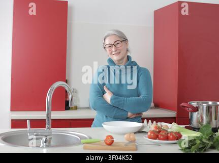 Selbstbewusste Seniorin, die in einer modernen roten Küche lächelt Stockfoto