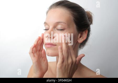 Junge Frau, die ihr Gesicht mit Feuchtigkeitscreme aufträgt Stockfoto