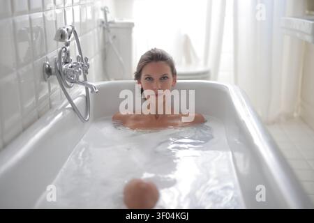 Frau, die in die Kamera schaut, während sie sich in der Badewanne entspannt Stockfoto