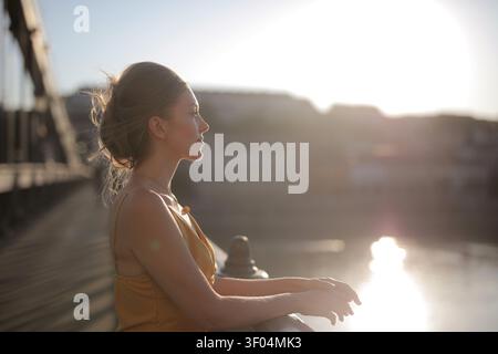 Frau im Profil genießt den Sonnenuntergang auf einer Brücke Stockfoto